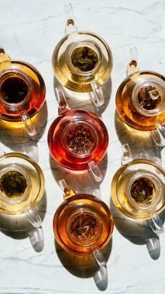 Top view of assorted herbal teas in glass teapots casting shadows on a marble surface.