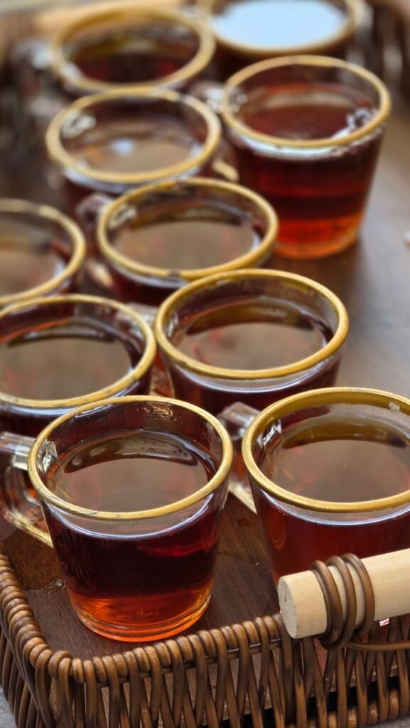 A collection of glass tea cups filled with tea on a wicker tray, featuring a honey stick.