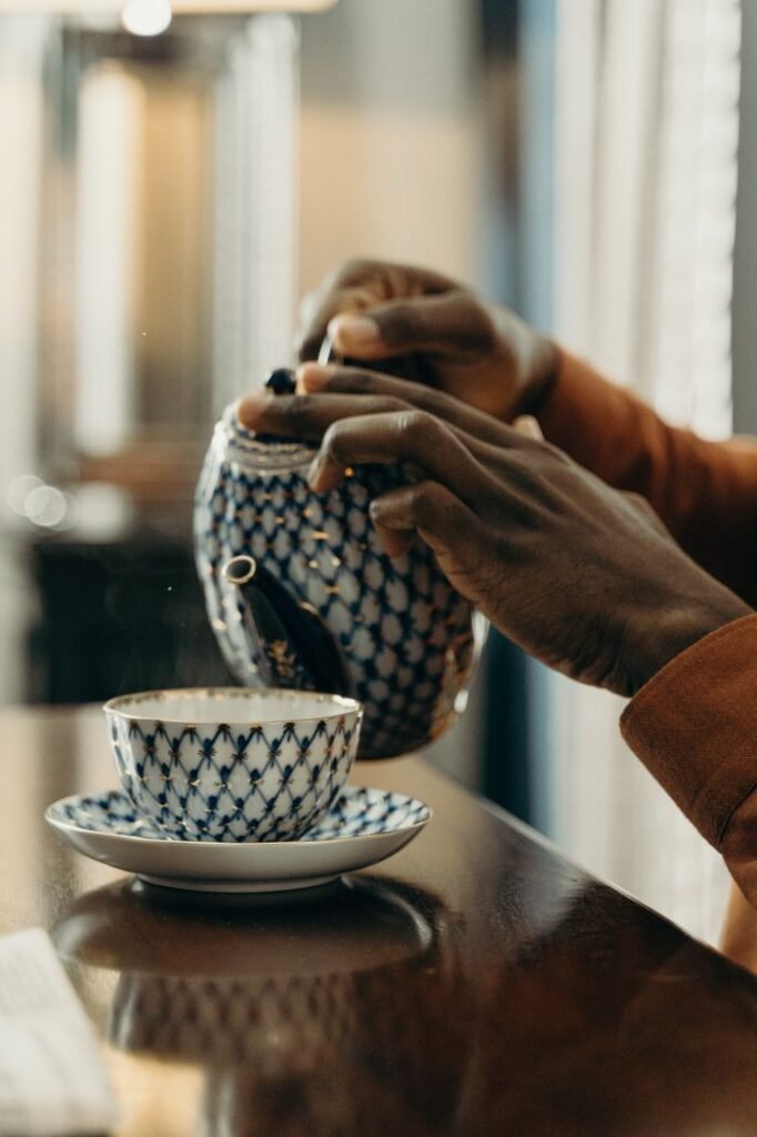 A person pours tea from a decorative teapot into a porcelain cup, captured in a cozy indoor setting.